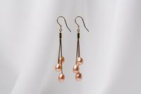 a pair of gold drop earrings with 3 pearls on a white background