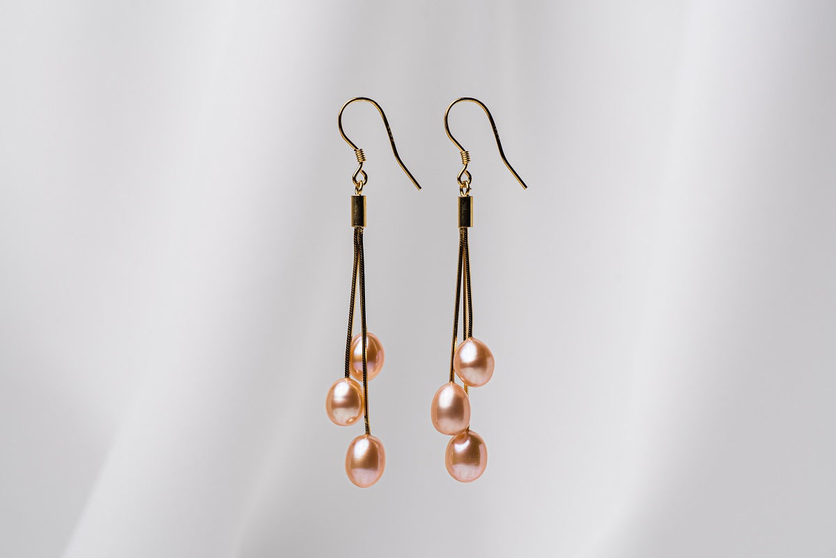 a pair of gold drop earrings with 3 pearls on a white background