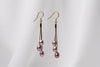 A pair of gold drop earrings with 3 lavender pearls on a white background