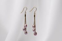 A pair of gold drop earrings with 3 lavender pearls on a white background