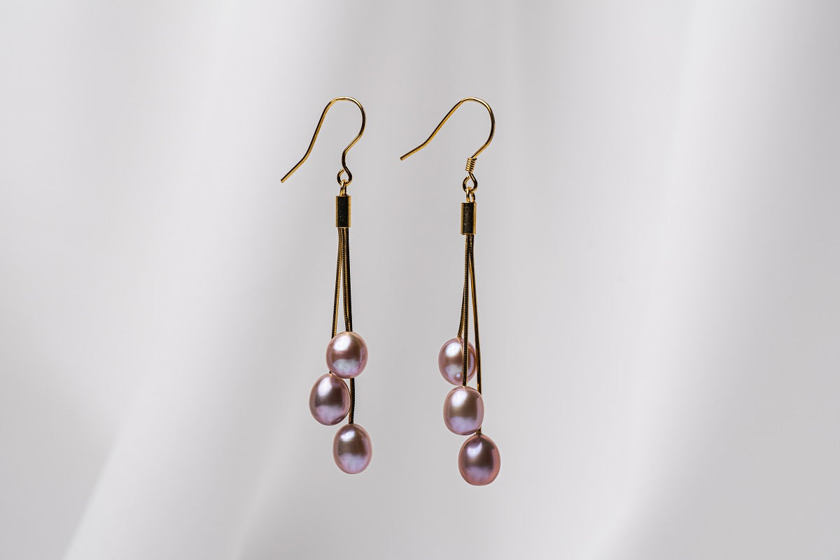 A pair of gold drop earrings with 3 lavender pearls on a white background