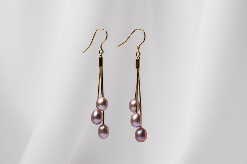 A pair of gold drop earrings with 3 lavender pearls on a white background