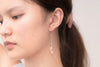 A close up of a model wearing a silver drop earring with 3 rose pearls.