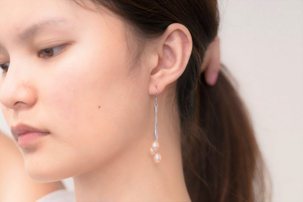 A close up of a model wearing a silver drop earring with 3 rose pearls.