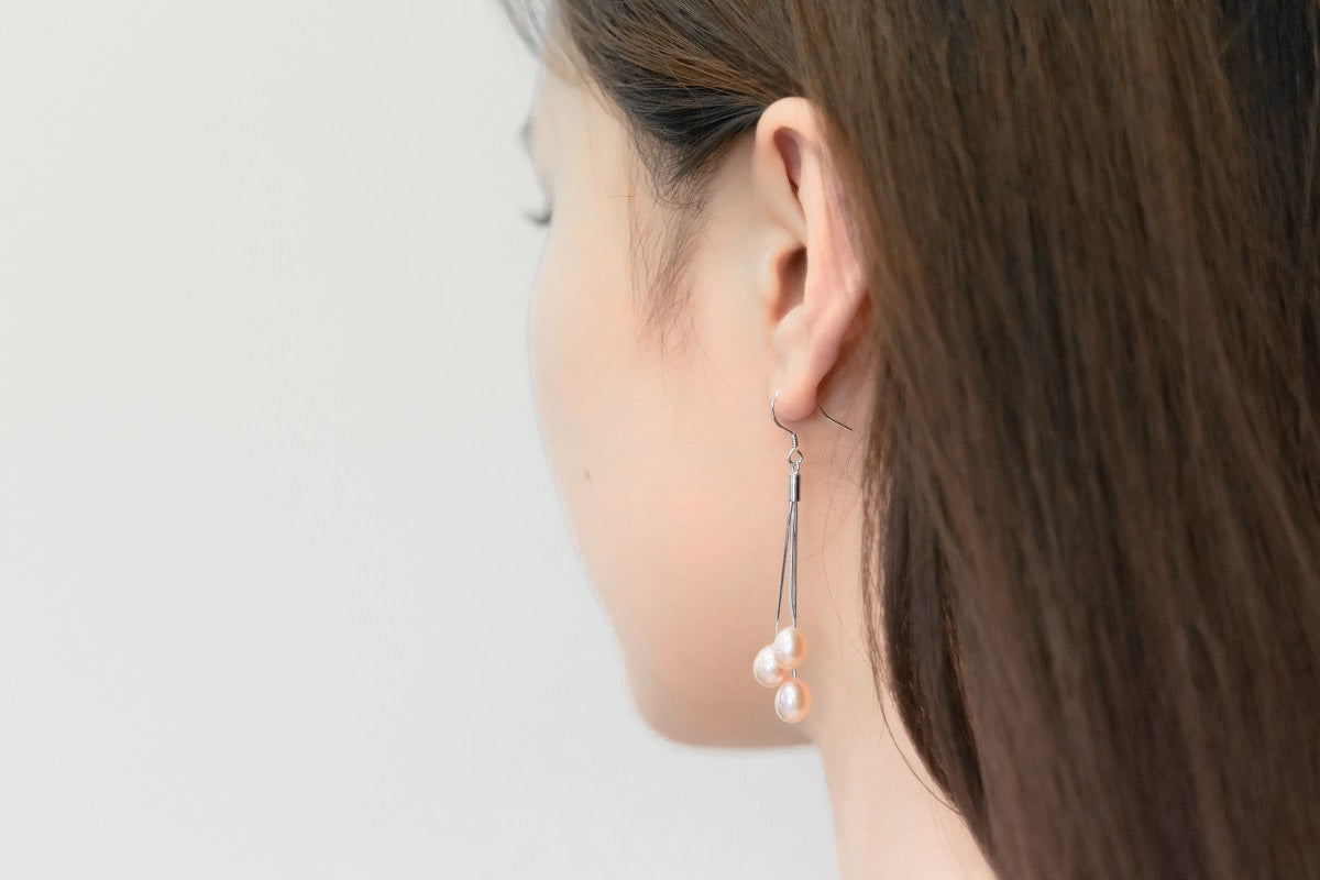A close up of a model wearing a silver drop earring with 3 rose pearls.