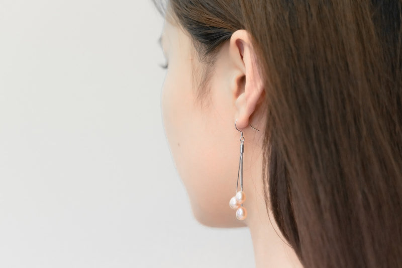 A close up of a model wearing a silver drop earring with 3 rose pearls.