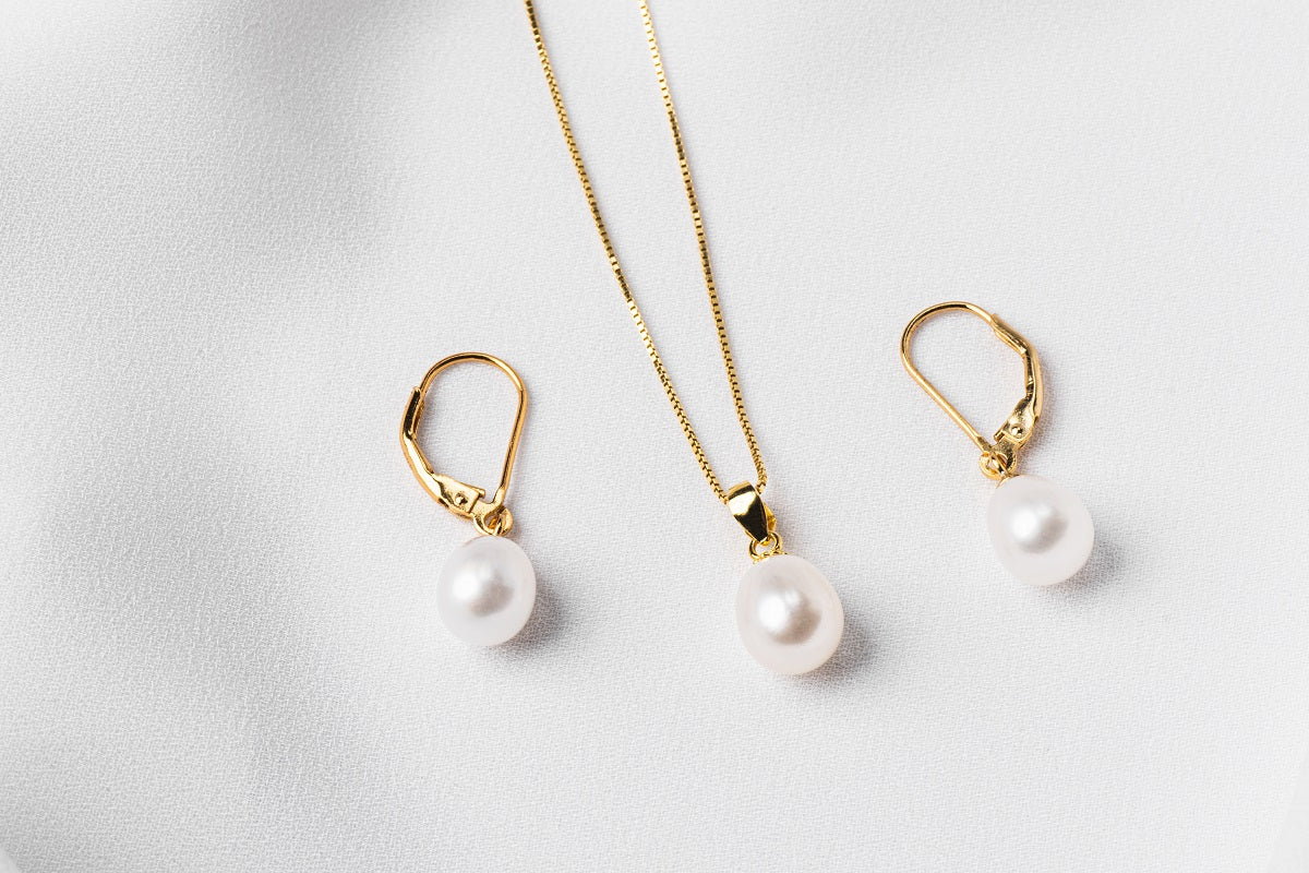 A set of jewelry including a necklace and earrings with white drop-shaped pearls, sterling silver and gold vermeil accents on a white background.