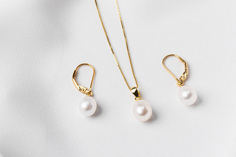 A set of jewelry including a necklace and earrings with white drop-shaped pearls, sterling silver and gold vermeil accents on a white background.