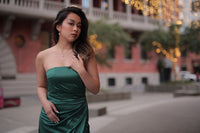 Asain woman in a green dress wearing a pearl necklace and pearl earrings set with a blurred background