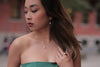 Asain woman in a green dress wearing a pearl necklace and pearl earrings set with a blurred background
