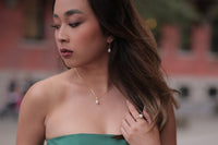 Asain woman in a green dress wearing a pearl necklace and pearl earrings set with a blurred background