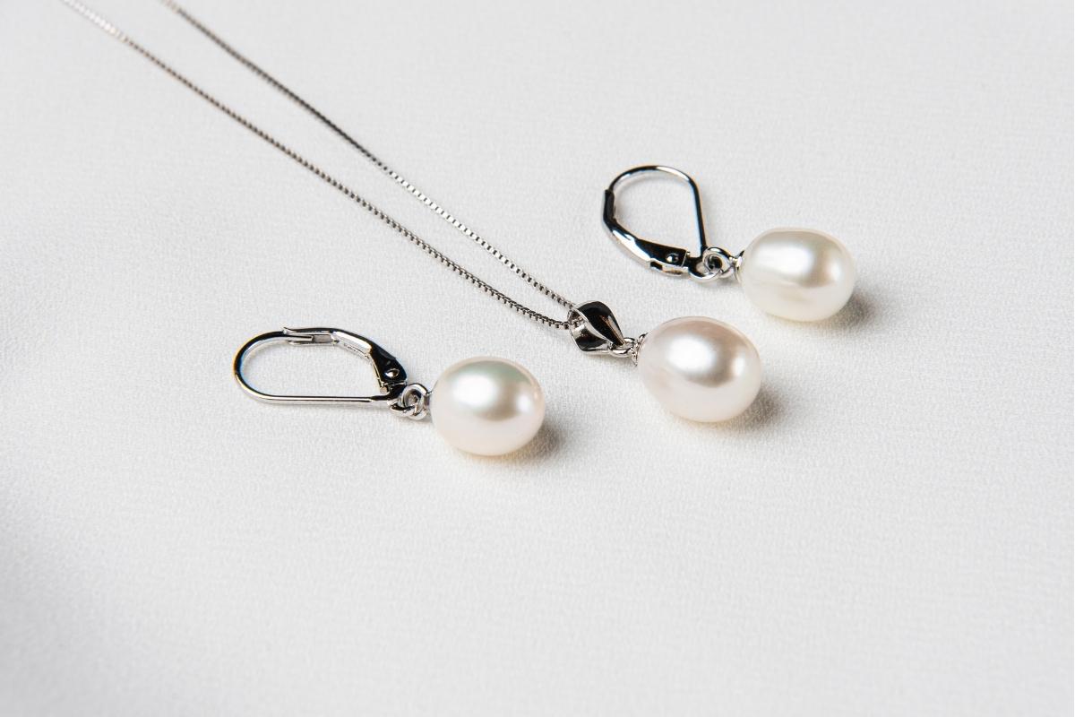 A set of jewelry including a necklace and earrings with white drop-shaped pearls, sterling silver on a white background.