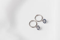 A pair of  huggies earring silver hoop adorned with a blue evil eye plate, displayed on a white background.