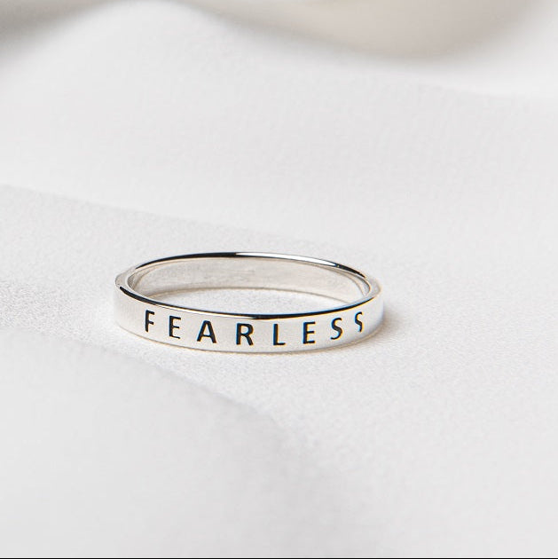 A silver ring with the word "FEARLESS" inscribed in to the band on a white surface.