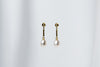 A pair of dangle earrings with a drop design, featuring pearl earrings and gold-colored metal backs, displayed against a white fabric background.