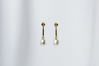 A pair of dangle earrings with a drop design, featuring pearl earrings and gold-colored metal backs, displayed against a white fabric background.