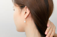 A pair of dangle earrings with a drop design, featuring pearl earrings and silver backs, displayed on a female model