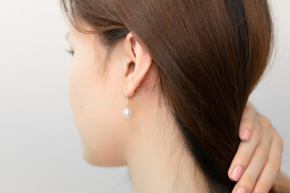 A pair of dangle earrings with a drop design, featuring pearl earrings and silver backs, displayed on a female model