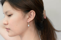 A pair of dangle earrings with a drop design, featuring pearl earrings and silver backs, displayed on a female model