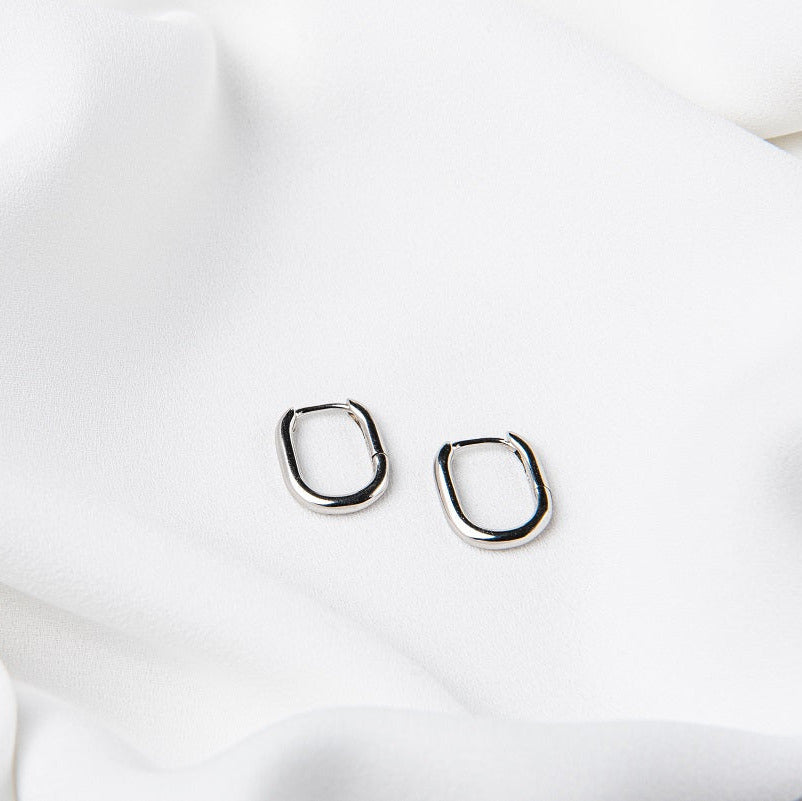 A pair of silver hoop earrings on a white fabric background.