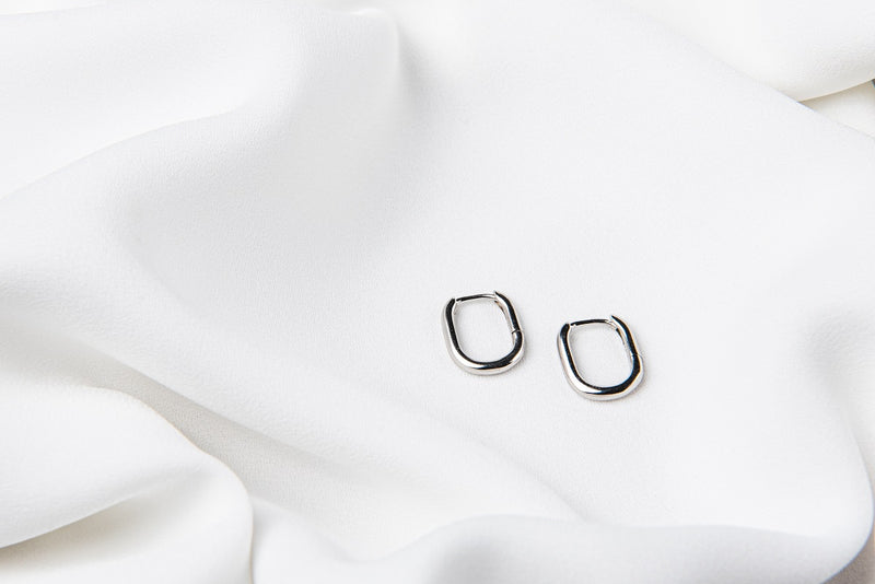 A pair of silver hoop earrings on a white fabric background.