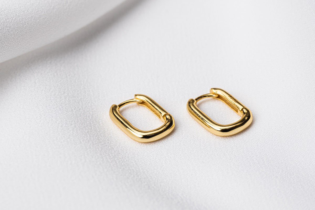 A pair of gold vermeil hoop earrings on a white fabric background.