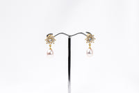 A pair of pearl earrings with butterfly backs and dangle design, featuring white pearls and a sparkling floral-shaped pendant in gold vermeil and diamond cubic zirconia.