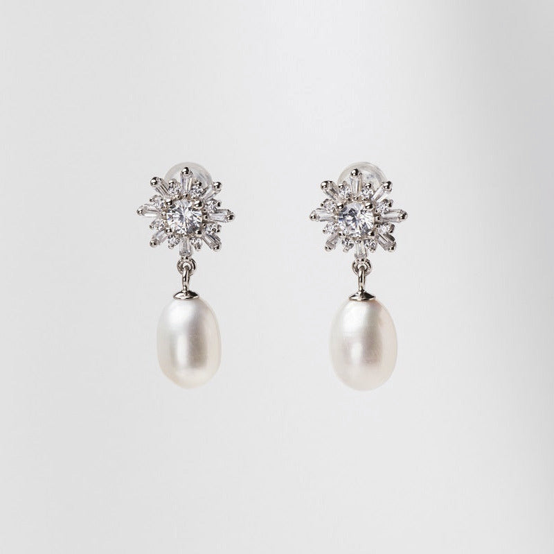 A pair of pearl earrings with butterfly backs and dangle design, featuring white pearls and a sparkling floral-shaped pendant and diamond cubic zirconia.