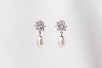 A pair of pearl earrings with butterfly backs and dangle design, featuring white pearls and a sparkling floral-shaped pendant and diamond cubic zirconia.