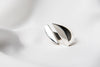 A polished, silver ring with a smooth, curved design positioned on a white surface.