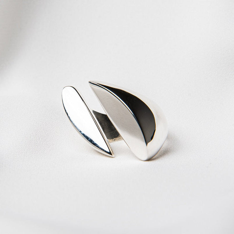 A polished, silver ring with a smooth, curved design positioned on a white surface.