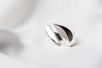 A polished, silver ring with a smooth, curved design positioned on a white surface.
