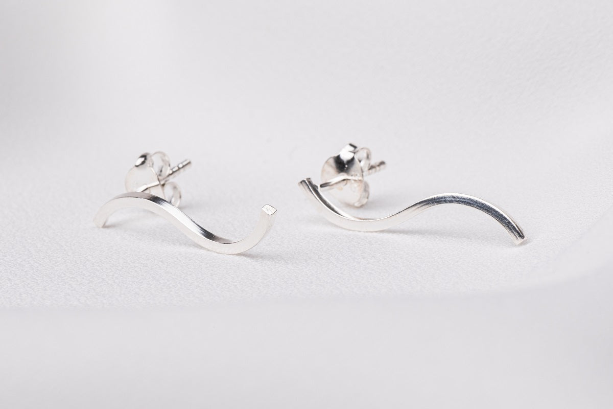 A pair of silver earrings in the shape of a curved line on a white background