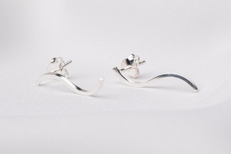 A pair of silver earrings in the shape of a curved line on a white background