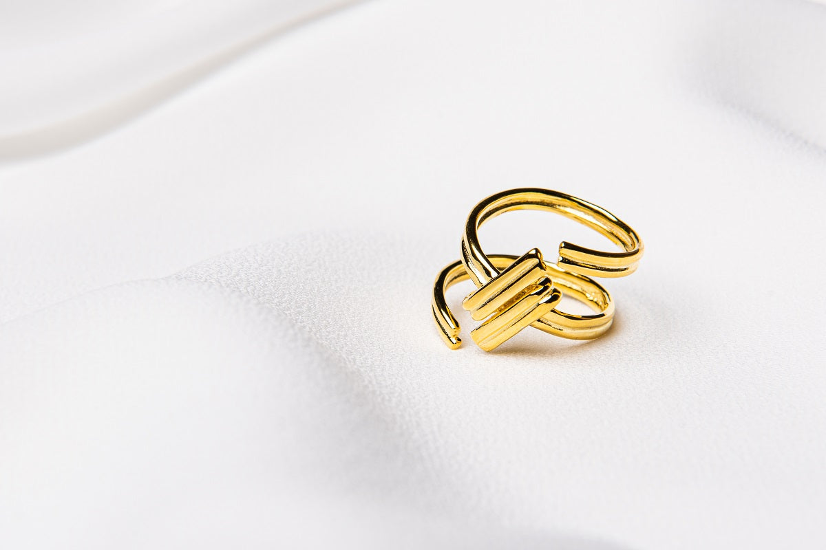 A gold ring with an adjustable band, in the shape of a hash tag placed on a white fabric surface.