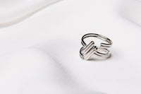 A silver ring with an adjustable band, in the shape of a hash tag placed on a white fabric surface.