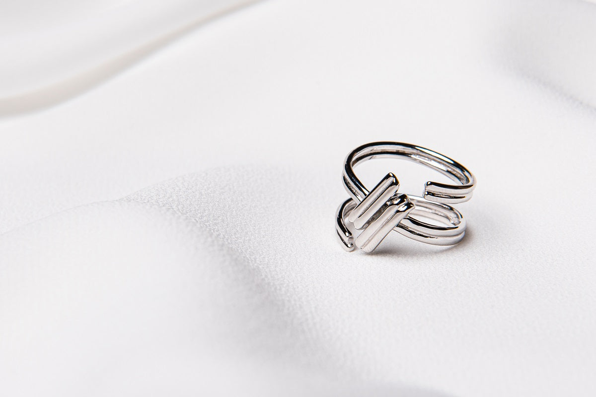 A silver ring with an adjustable band, in the shape of a hash tag placed on a white fabric surface.