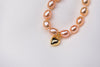 A sterling silver and gold vermeil champagne pearl necklace with a potato-shaped pearl drop and a gold heart-shaped clasp, displayed on a white fabric surface.