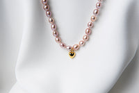 A sterling silver and gold vermeil lavender pearl necklace with a potato-shaped pearl drop and a heart-shaped clasp, displayed on a white fabric surface.