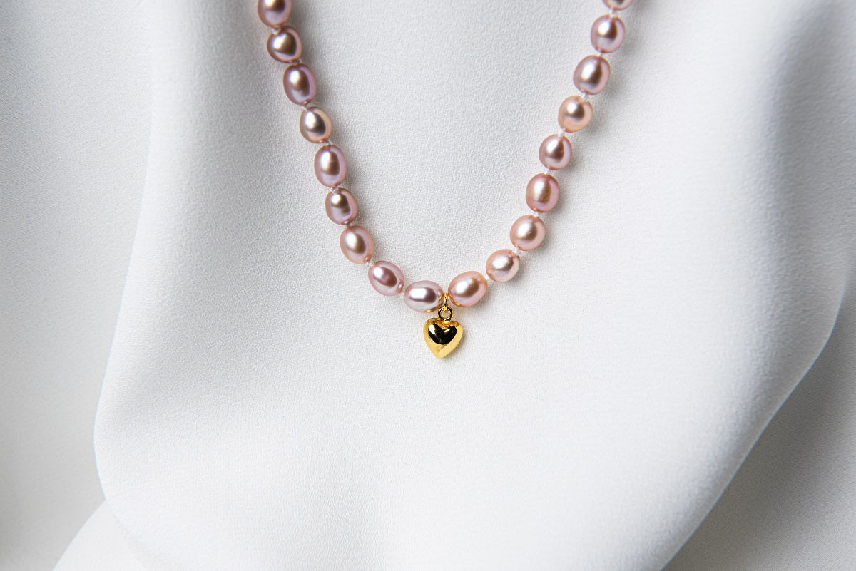 A sterling silver and gold vermeil lavender pearl necklace with a potato-shaped pearl drop and a heart-shaped clasp, displayed on a white fabric surface.