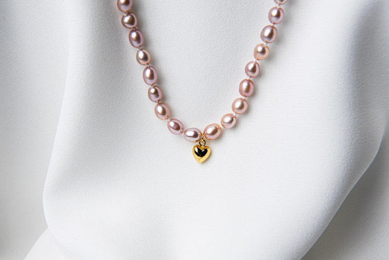 A sterling silver and gold vermeil lavender pearl necklace with a potato-shaped pearl drop and a heart-shaped clasp, displayed on a white fabric surface.