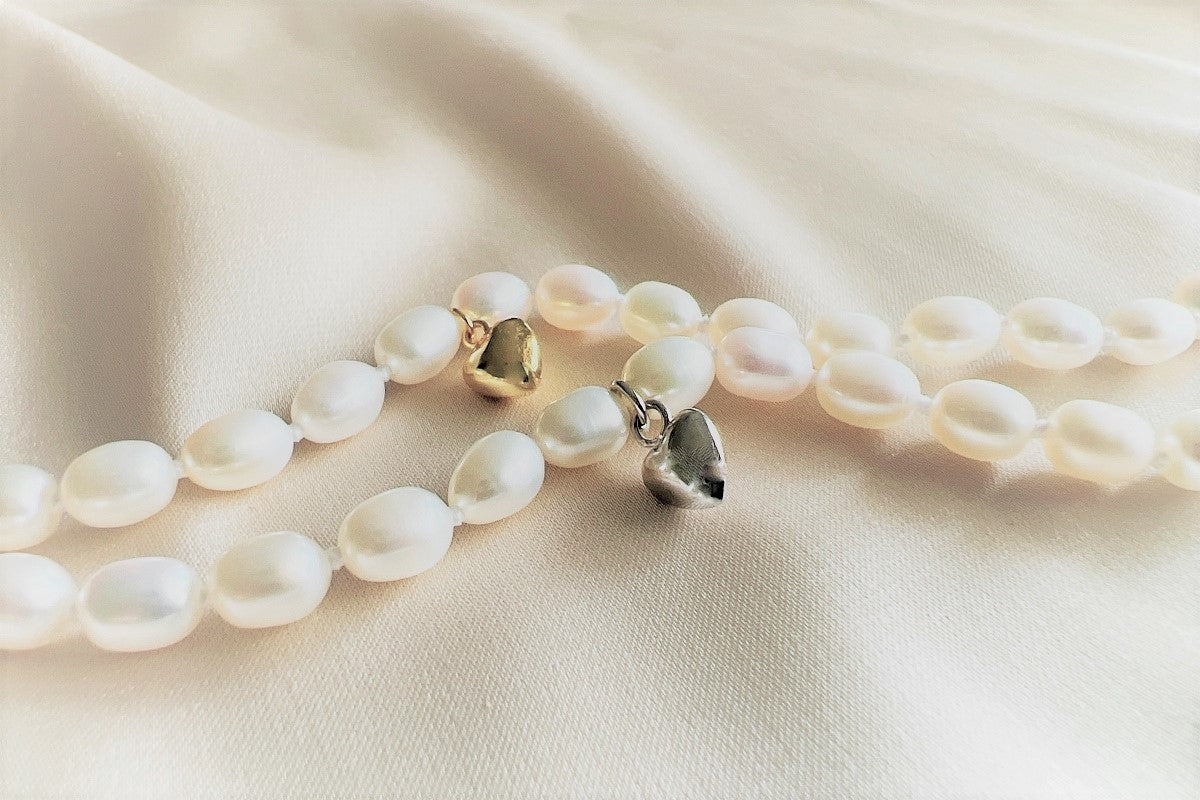 A sterling silver and gold vermeil white pearl necklace with a potato-shaped pearl drop and a heart-shaped clasp, displayed on a white fabric surface.