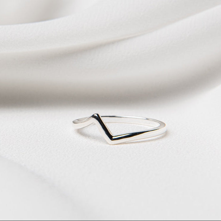 A silver ring with a heartbeat-like pattern on its top surface, placed on a white fabric background.