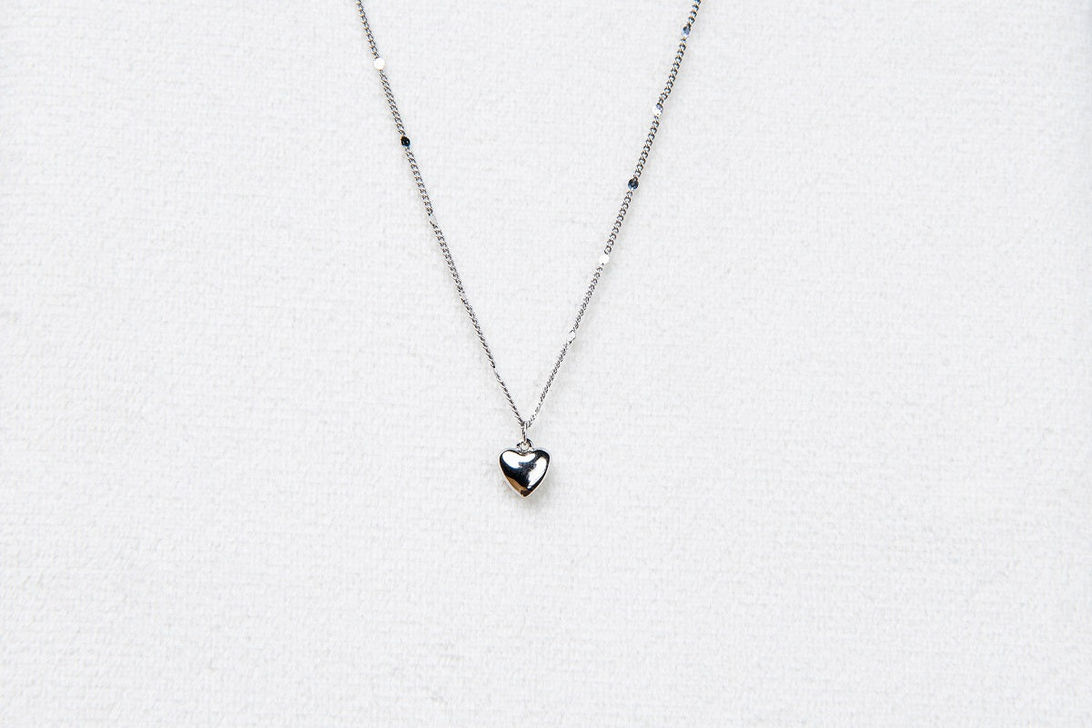 A silver chain necklace with a small heart penant on a white background.