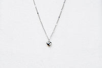 A silver chain necklace with a small heart penant on a white background.