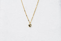 A gold chain necklace with a small heart penant on a white background.