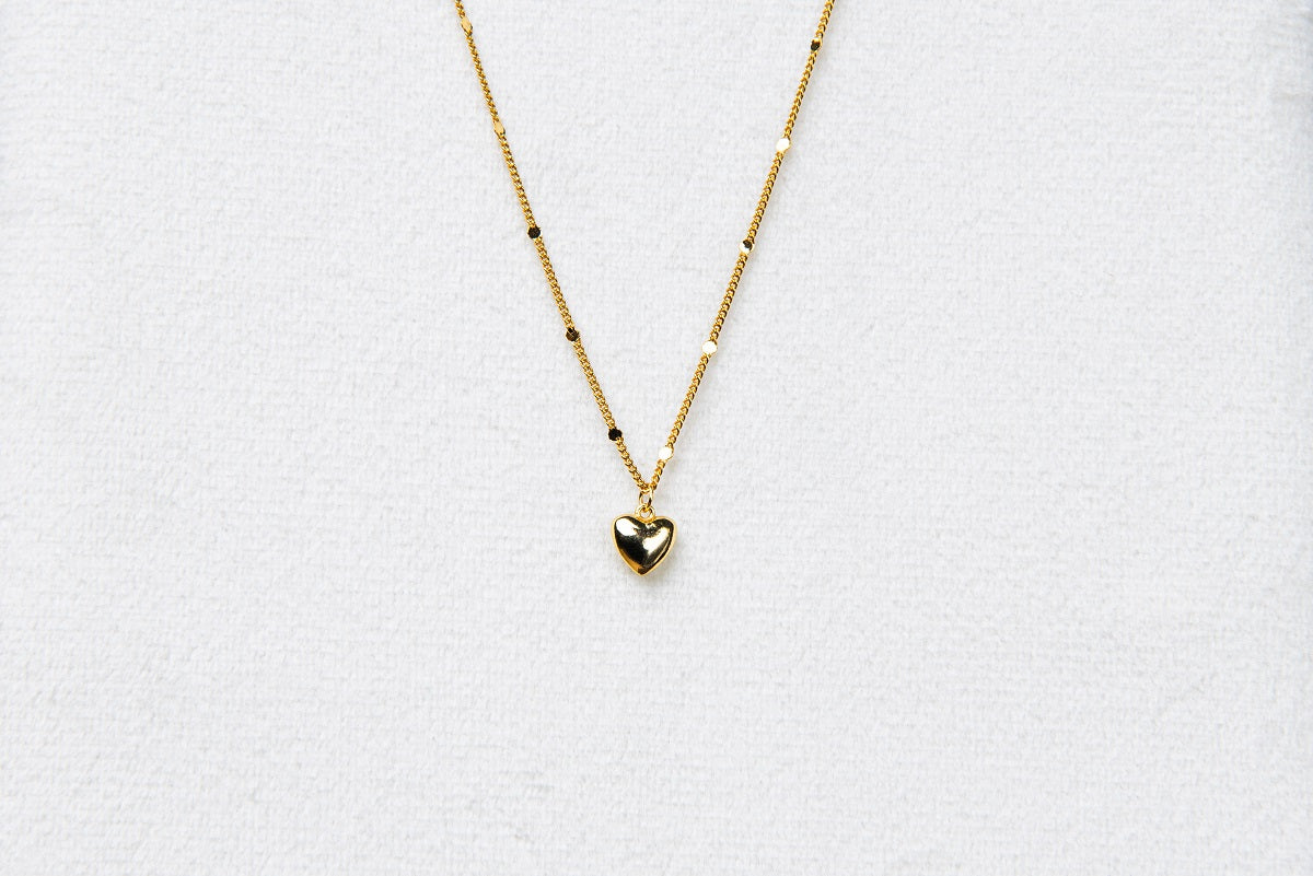 A gold chain necklace with a small heart penant on a white background.