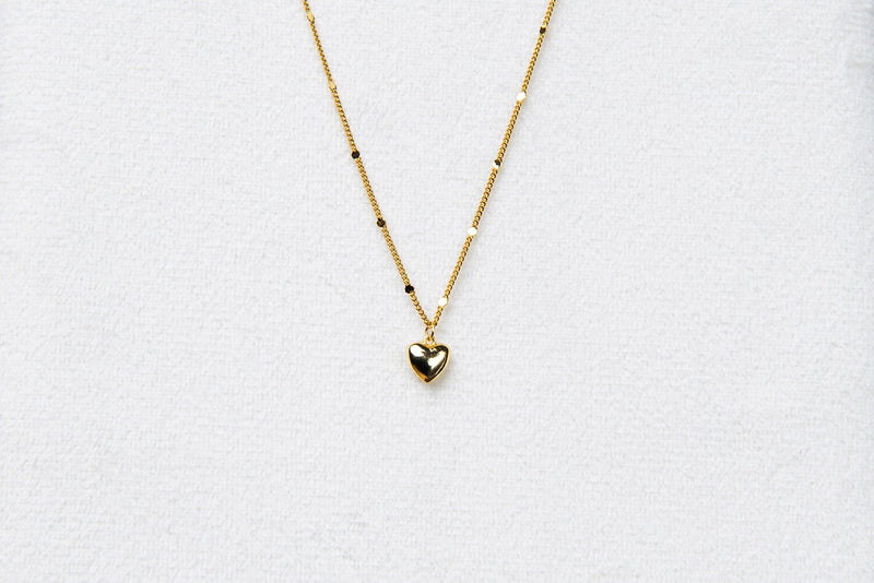 A gold chain necklace with a small heart penant on a white background.