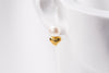 A close-up image of a single pearl earring with a gold vermeil heart drop deisplayed on a white mannequine.