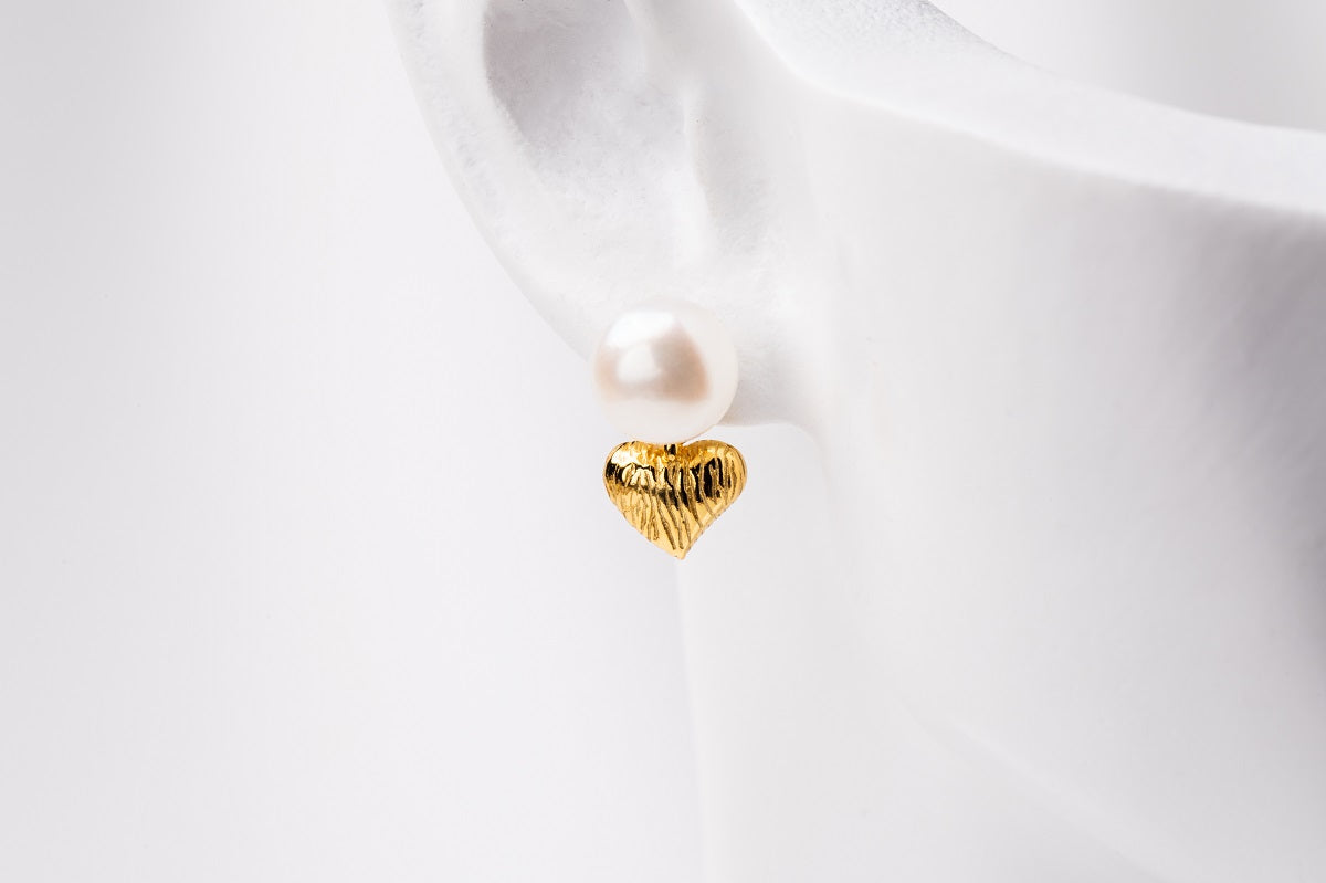 A close-up image of a single pearl earring with a gold vermeil heart drop deisplayed on a white mannequine.